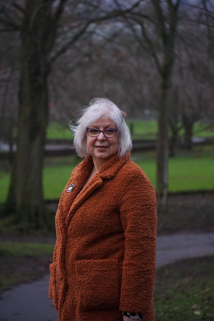 Rosalind Fairclough standing outside in an orange coat, with trees behind her.